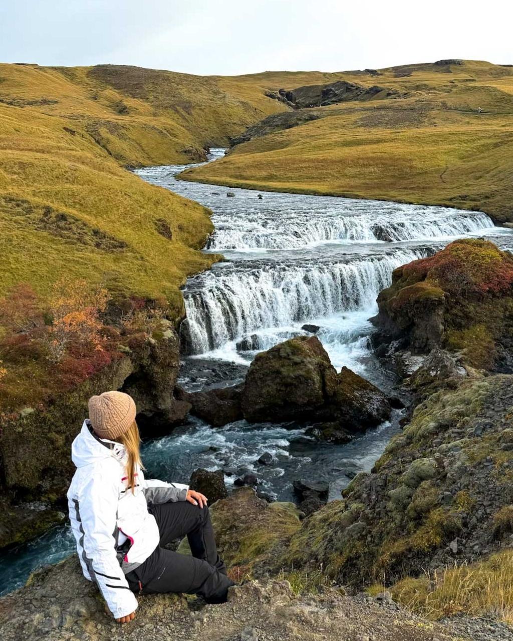 ragazza seduta su una roccia che guarda una cascata. Itinerario di 7 giorni in Islanda